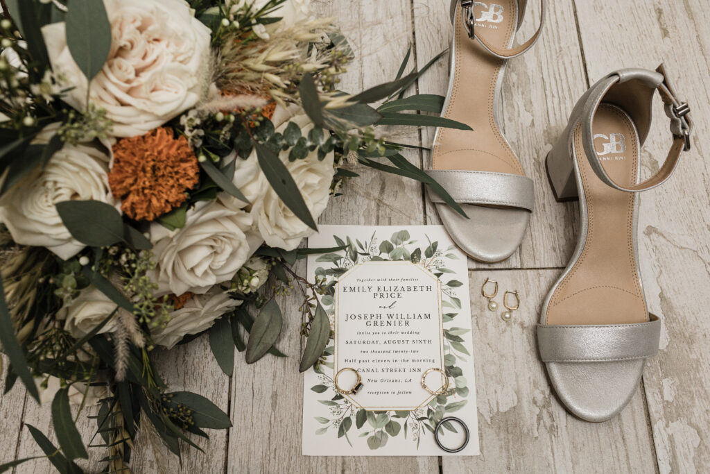 Bouquet, bridal shoes, and wedding rings surround a wedding invitation